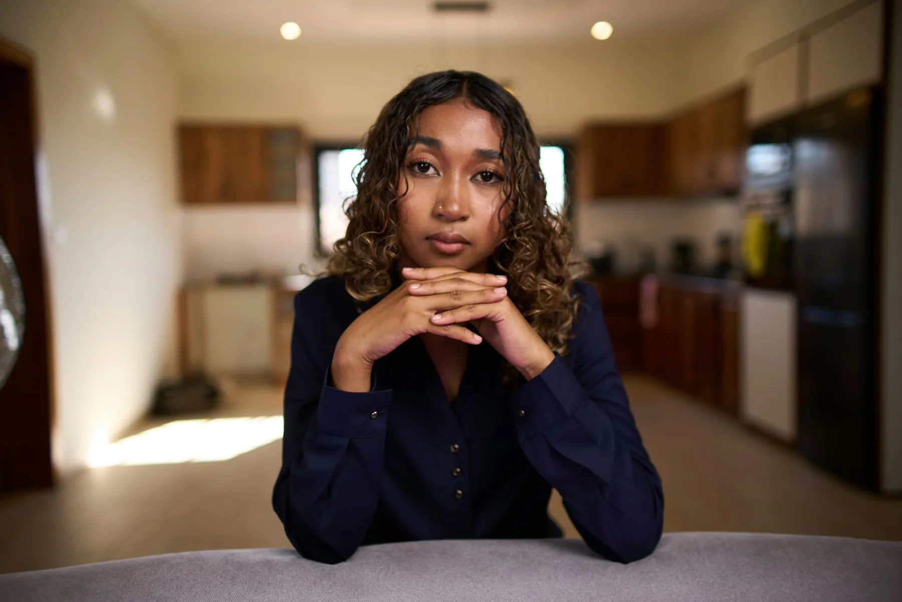 A woman sitting at a kitchen table, looking towards the camera